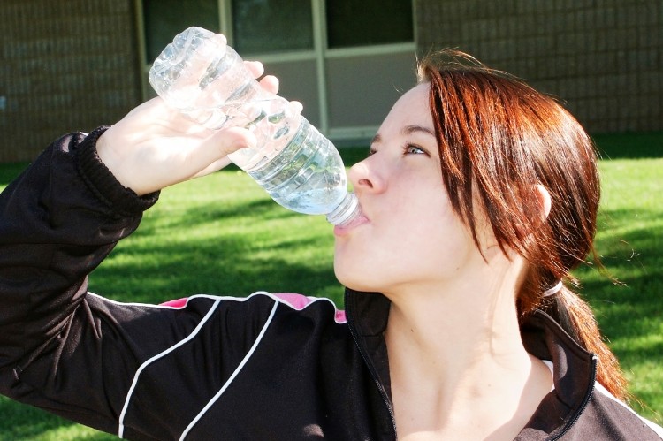 hnědovlasá žena ve sportovním oblečení, která pije vodu z lahve