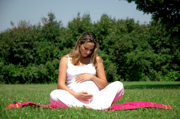 těhotná žena sedící venku na růžové jógové podložce