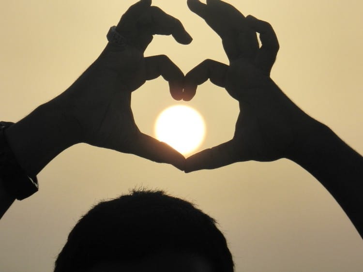 lidské ruce spojené do srdce v pozadí se sluncem